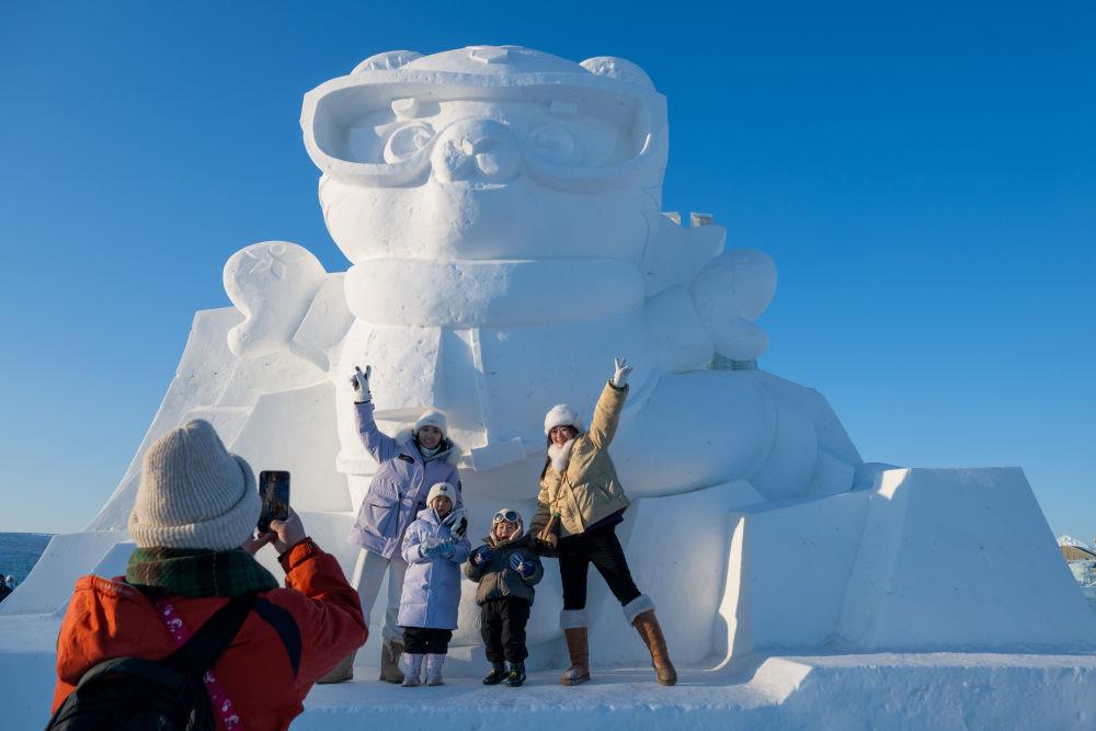 2025年1月3日，在黑龙江哈尔滨冰雪大世界园区，游客与亚冬会吉祥物雪雕“滨滨”合影